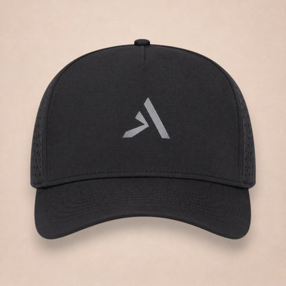 Noir hat, front view, all black with perforated side panels and a grey A logo on the crown, on a plain beige background.