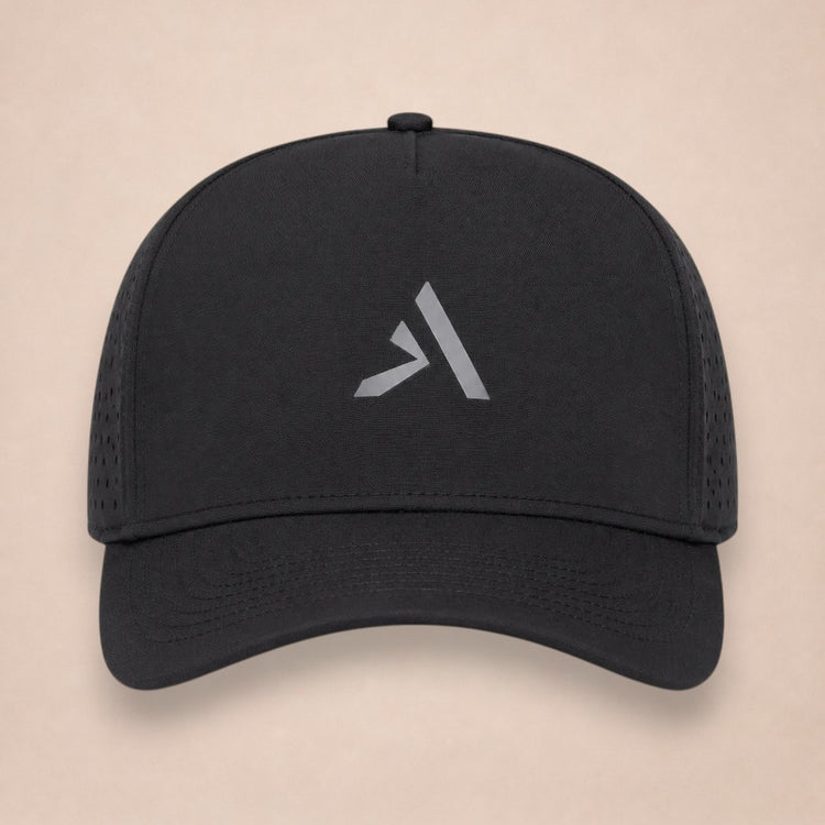 Noir hat, front view, all black with perforated side panels and a grey A logo on the crown, on a plain beige background.