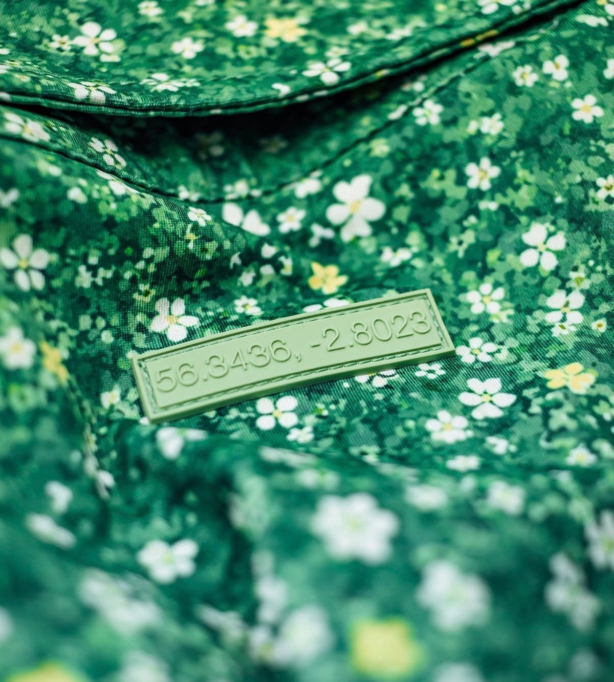 The debossed coordinate patch below the collar of a Proving Ground polo in Perennial